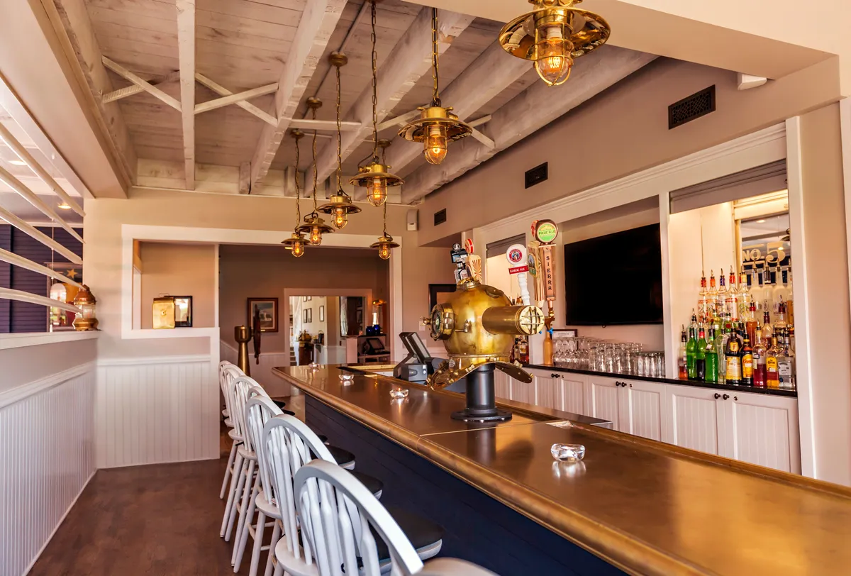 A stylish interior bar area featuring a sleek bar counter, hanging lights, shelves filled with bottles, and modern decorative elements. The space exudes a cheerful and relaxed vibe, inviting guests to gather and unwind after a day of adventure.