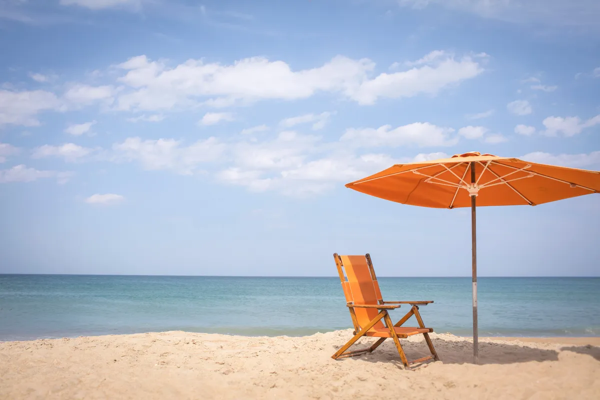 A serene beachfront setting featuring classic beach chairs and umbrellas set up on soft sand, with the tranquil ocean stretching out under a pastel sky. The setting is peaceful, inviting guests to relax, sunbathe, or enjoy quiet time together with unobstructed views of the water.